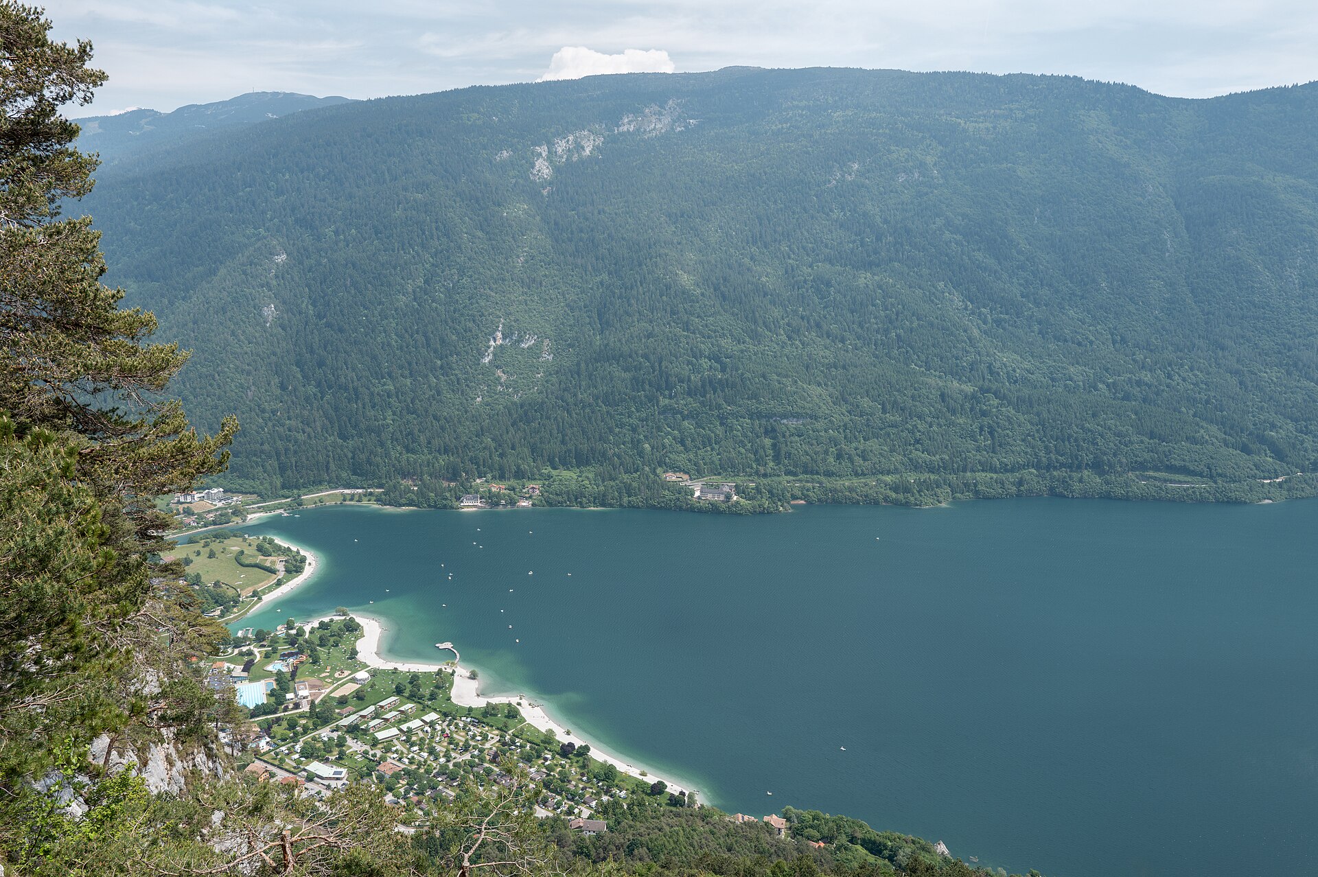 Lake Molveno lido and beaches seen from above beneath forested mountains